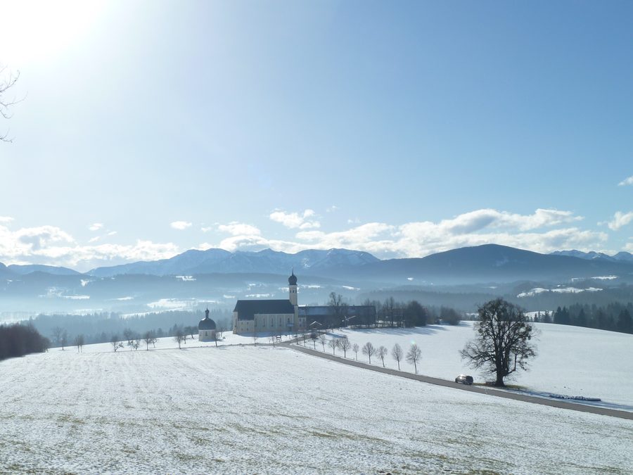 Wallfahrtskirche Wilparting an einem sonnigen Wintertag vor den Mangfallgebirgen