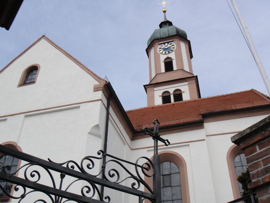 Turm und Schiff der Pfarrkirche St. Michael in Apfeltrang hinter dem geschmiedeten Friedhofstor