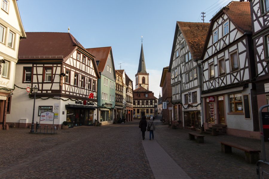 Gepflasterte Altstadtstraße mit Fachwerkhäusern und Kirchturm in Bayern.